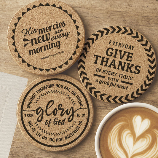 Three cork coasters with Christian Bible verses on a wooden surface with a cup of coffee and napkin.