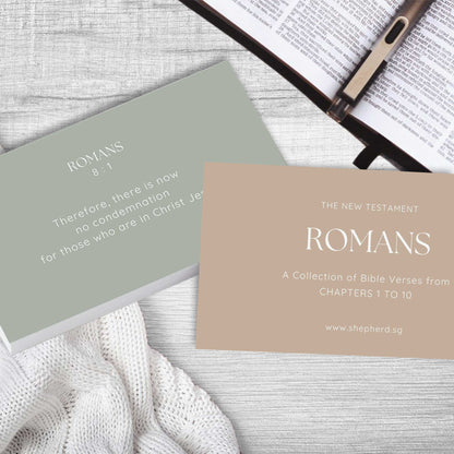 two cards with bible verse Romans on a bible and wooden top