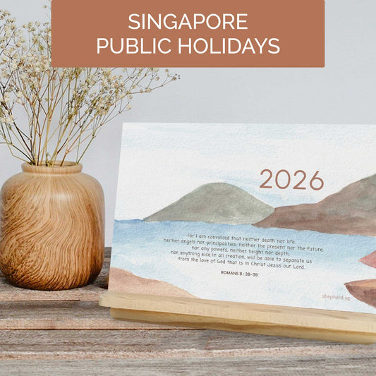 2026 calendar with bible verses and singapore public holidays on a wooden surface next to a vase.