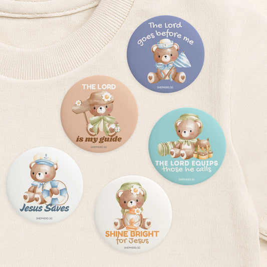 Set of teddy bear-themed pin badges with Bible truths on a cream shirt.