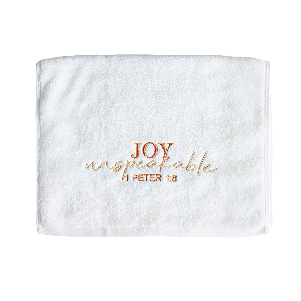 Folded white cotton towel with embroidered text 'Joy unspeakable 1 Peter 1:8' on a white background