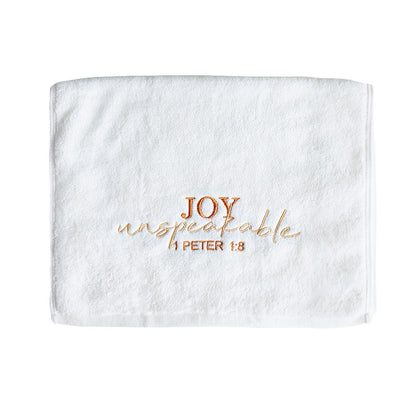 Folded white cotton towel with embroidered text 'Joy unspeakable 1 Peter 1:8' on a white background