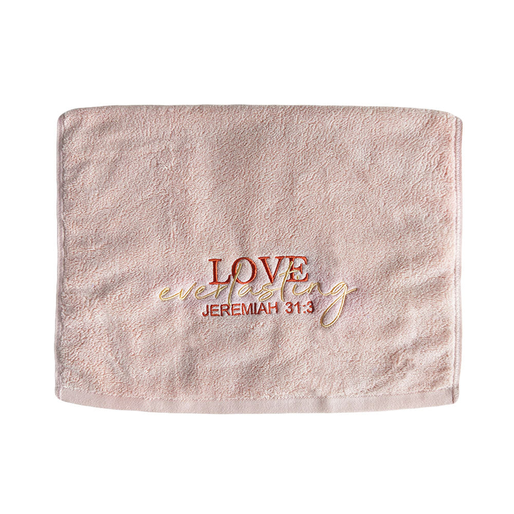 Folded rose pink cotton towel with embroidered text 'Love everlasting Jeremiah 31:3' on a white background