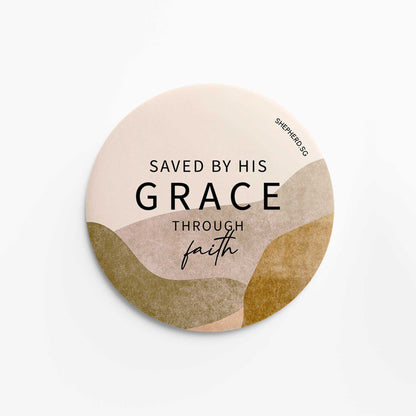 Round pin badge with 'Saved by His Grace Through Faith' text on a beige abstract background