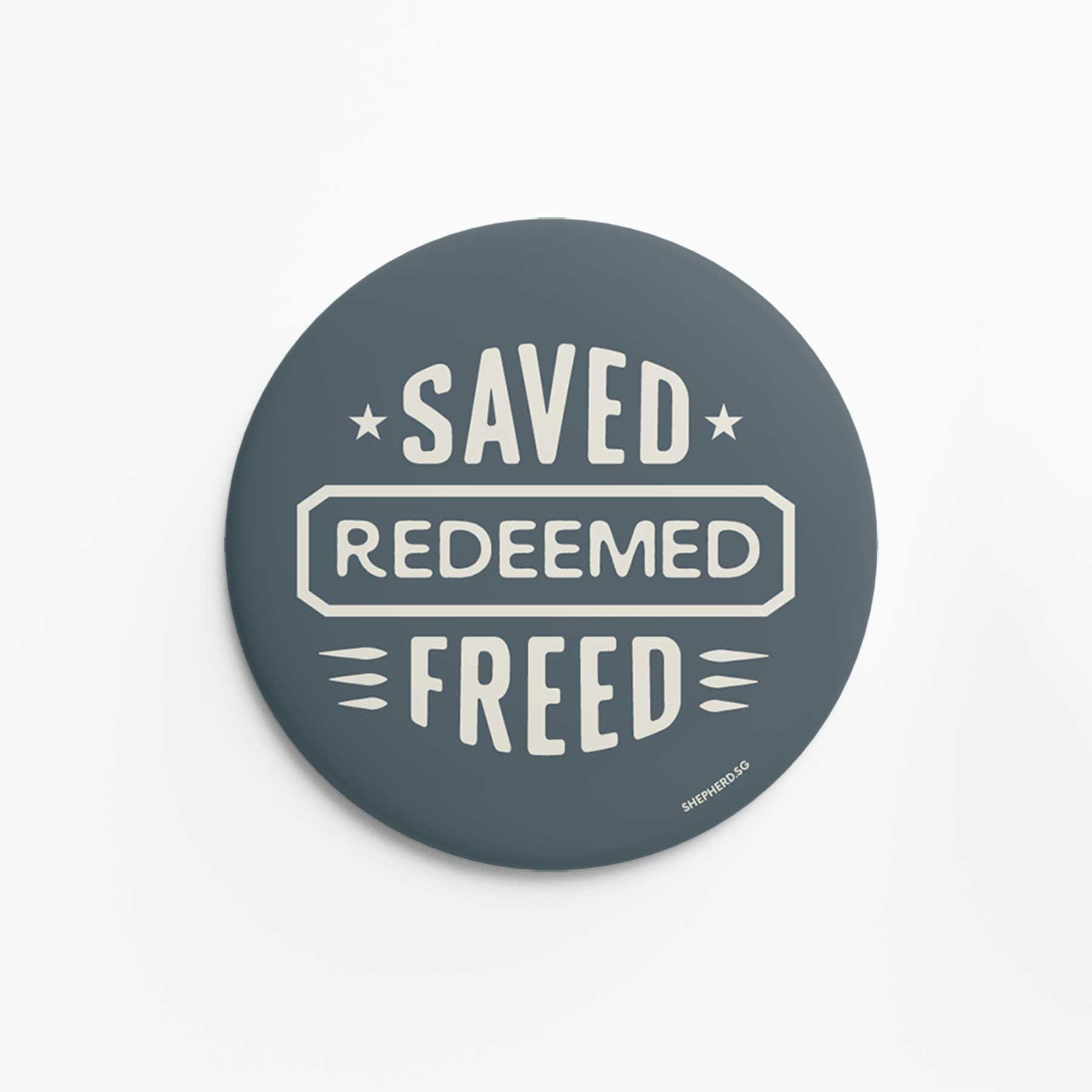 Round dark blue pin badge with 'Saved Redeemed Freed' text on a white background
