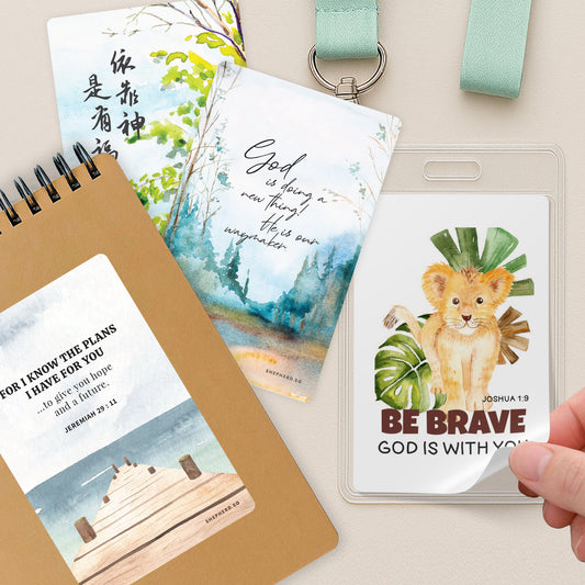 Stickers designed by Shepherd.SG displayed on a notebook, lanyard and individual pieces on a beige table top.