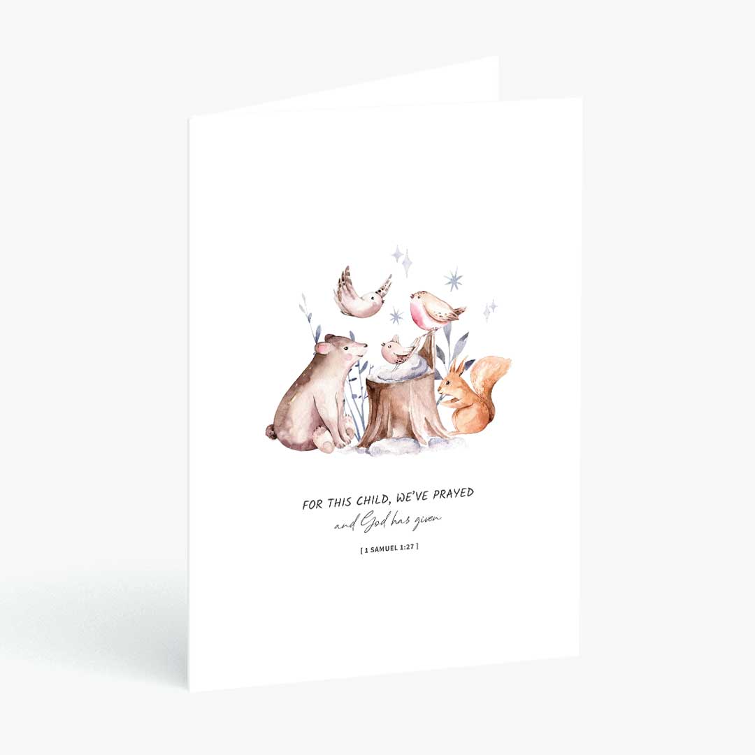 A white greeting card standing upright against a light gray background, featuring a watercolor illustration of woodland animals including a bear, fox, bird, and crescent moon, with the text 'FOR THIS CHILD, WE'VE PRAYED and God has given'.