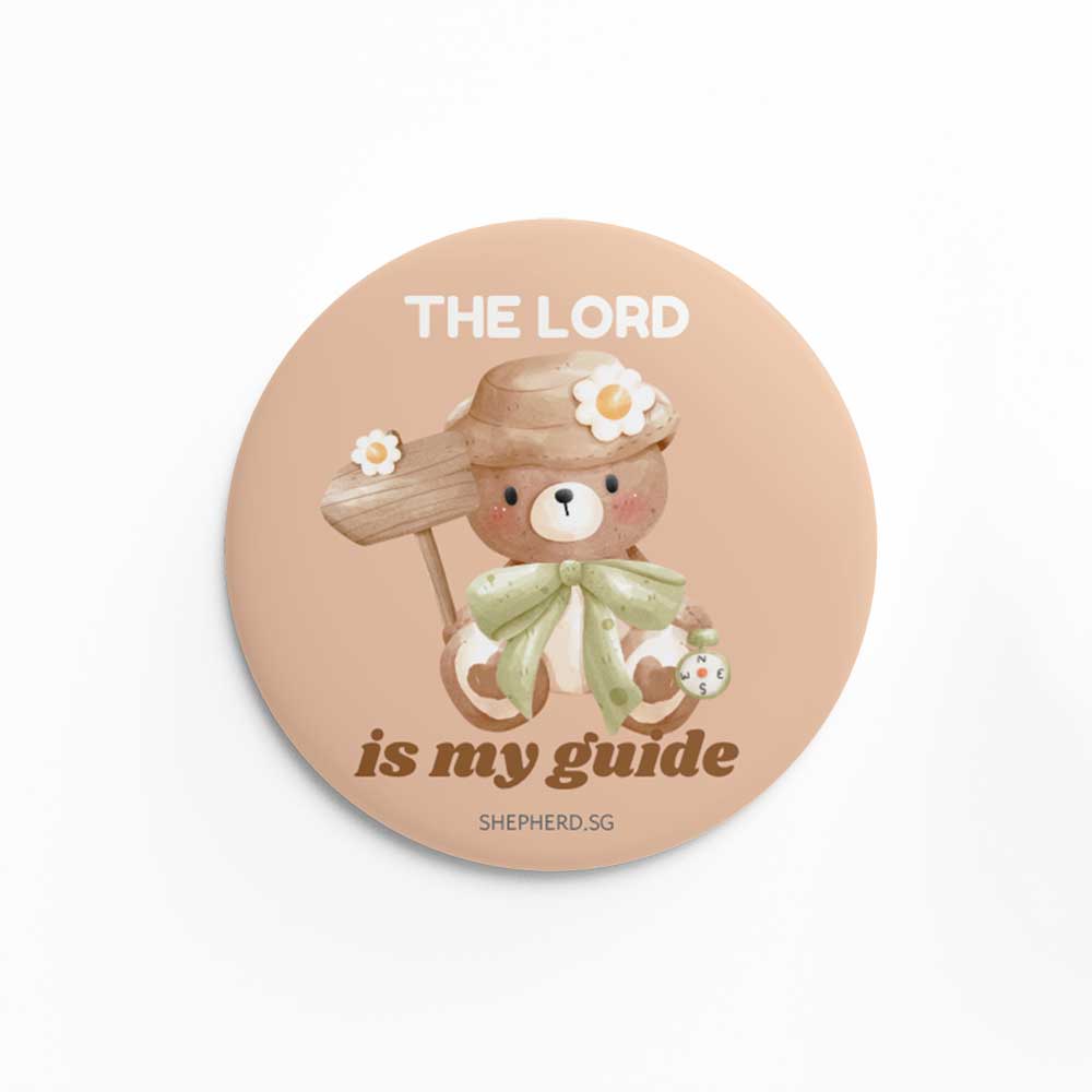 Button pin badge with teddy bear design holding a sign postand 'The Lord is my guide' text on a white background
