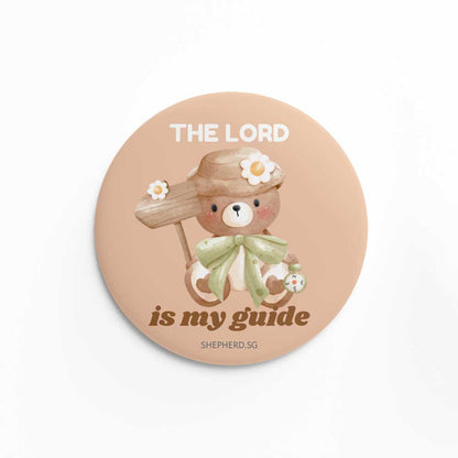 Button pin badge with teddy bear design holding a sign postand 'The Lord is my guide' text on a white background