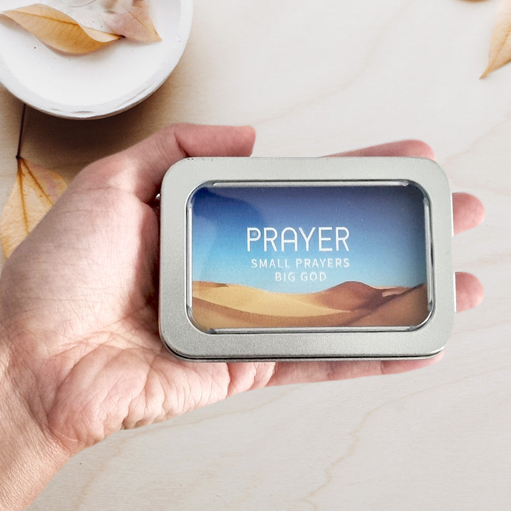 christian prayer cards in tin box held by a hand with rustic leaves in the background